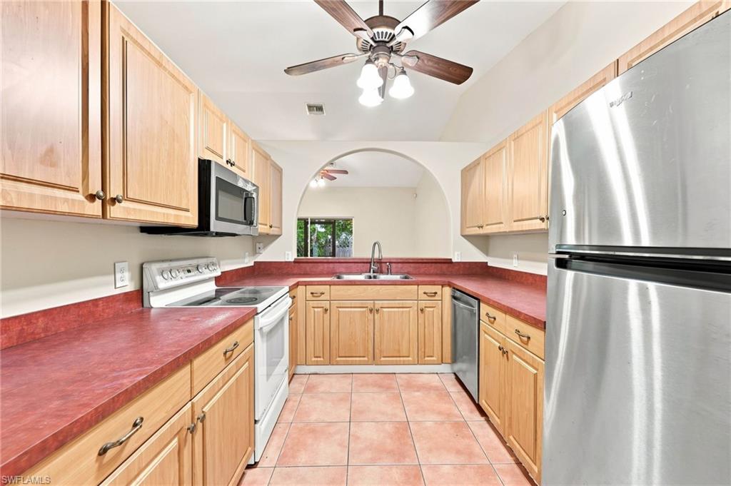Kitchen featuring wood cabinetry, red countertops, tile flooring, and vaulted ceiling