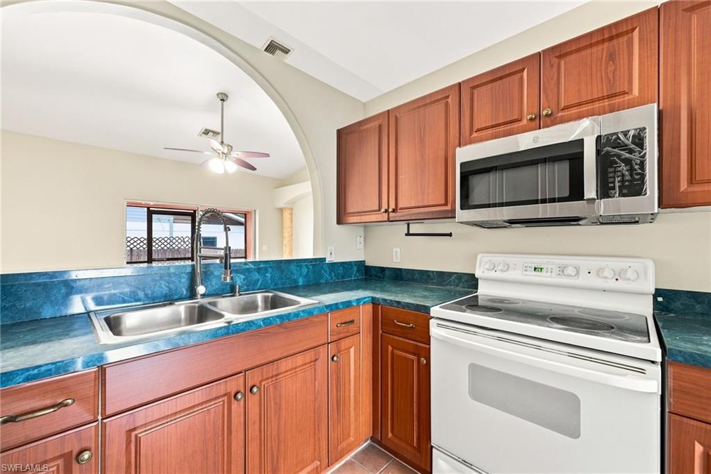 Kitchen featuring wood cabinetry, blue countertops, dual basin stainless steel sink with a high-arc faucet, white electric range, and a stainless steel over-the-range microwave