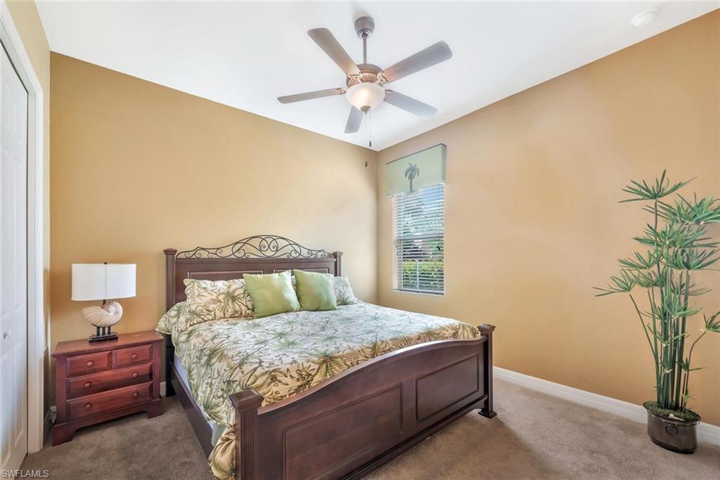 Carpeted bedroom with a wood-finish bed frame featuring an ornate headboard, a ceiling fan with integrated lighting, and a window with blinds