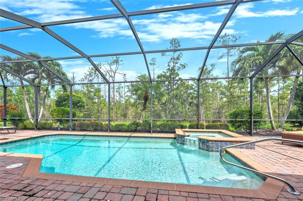 Screened pool enclosure featuring a rectangular swimming pool, integrated spa, and brick paver decking