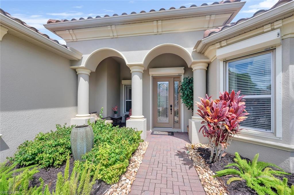 Arched portico entry featuring columns, a decorative glass front door, and a paver walkway