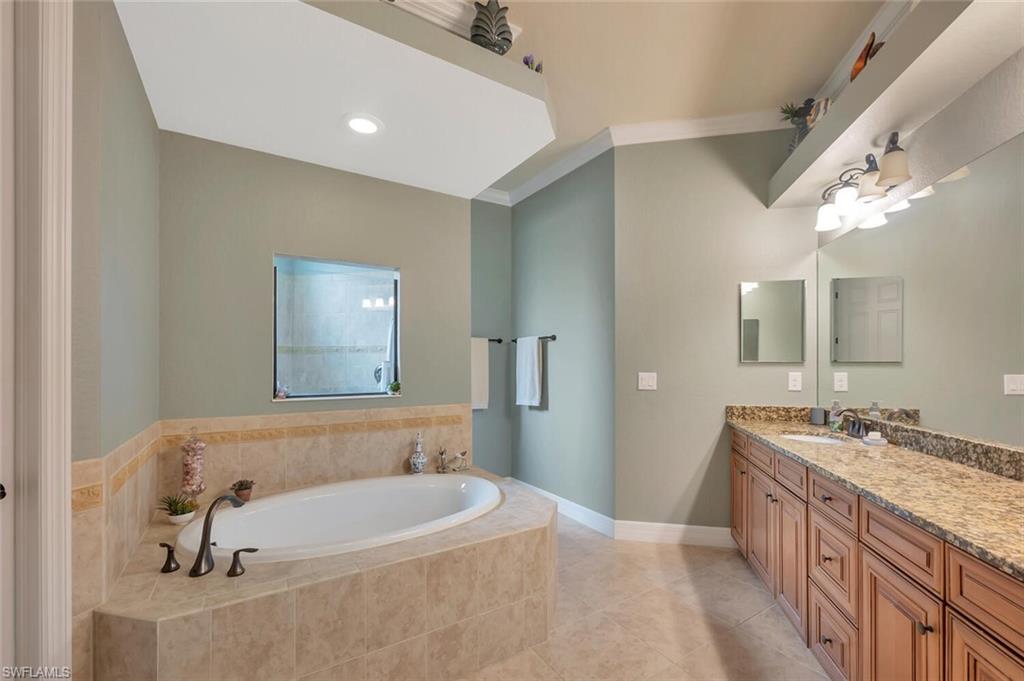 Bathroom featuring a large soaker tub with bronze fixtures, a tiled surround, and an integrated window
