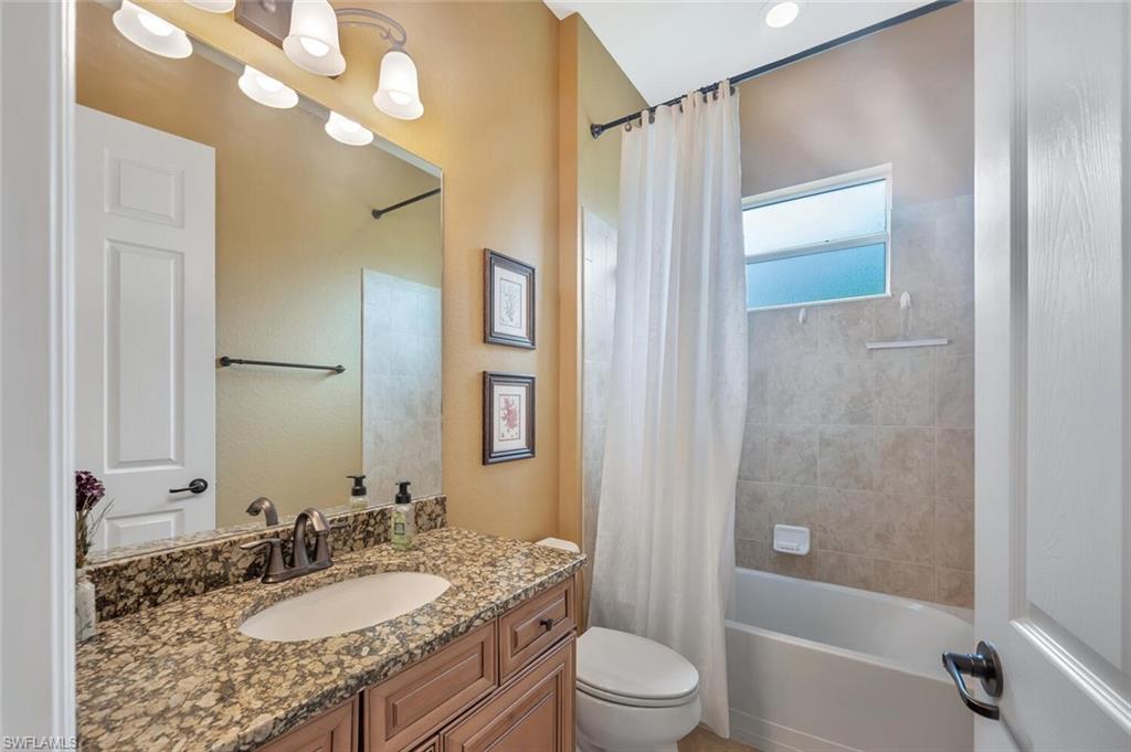 Bathroom featuring a granite-look countertop, wood-finish cabinetry, a single basin sink, and a tiled shower/tub combination with a privacy window