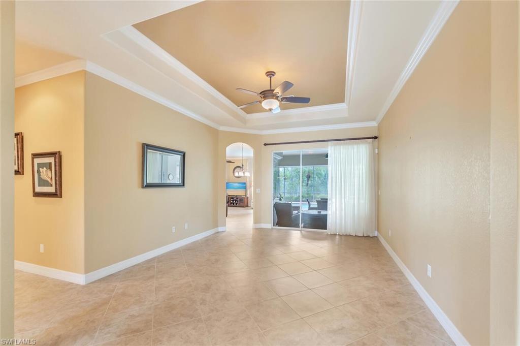 Expansive living area featuring large format tile flooring, a tray ceiling with crown molding, and a ceiling fan