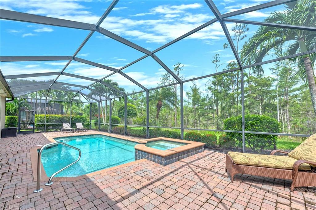 Screened pool enclosure featuring a rectangular pool, integrated spa, and brick paver decking