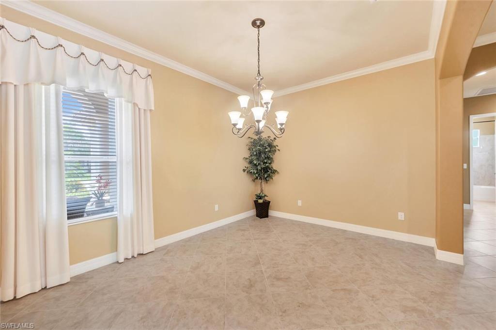 Spacious room featuring neutral wall tones, crown molding, a multi-bulb chandelier, large window with blinds, and tile flooring