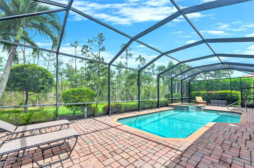 Screened-in outdoor pool area featuring a rectangular swimming pool with integrated spa, a paver deck, and lush perimeter landscaping