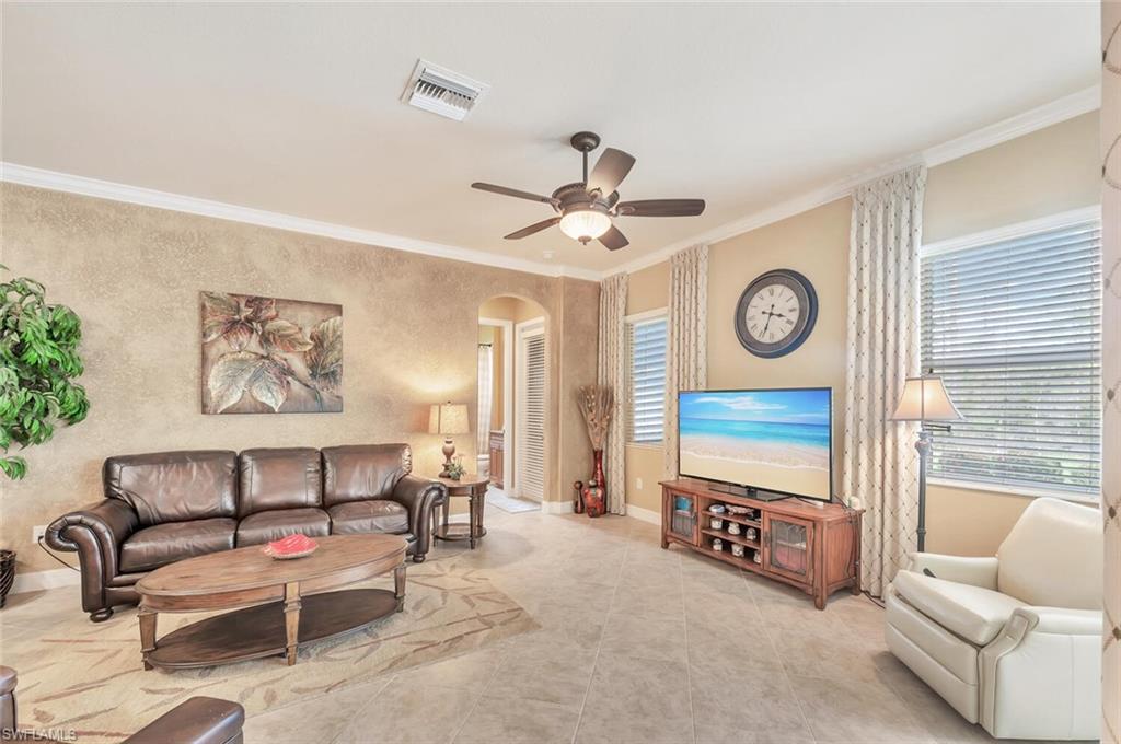 Spacious living area featuring light-toned tile flooring, crown molding, and a ceiling fan