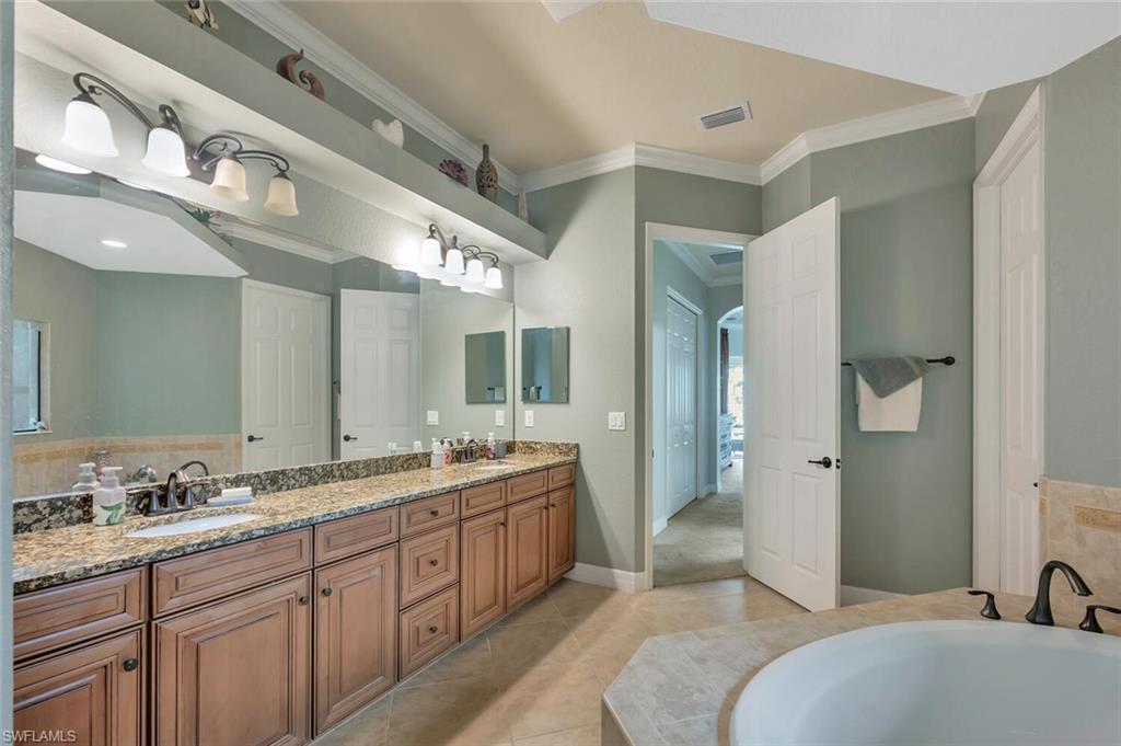 Bathroom featuring a dual vanity with wood cabinetry and a granite countertop, a full-width mirror, and a built-in garden tub