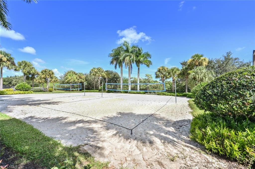 Sand volleyball court with two nets, surrounded by mature palm trees and lush landscaping, set under a clear blue sky