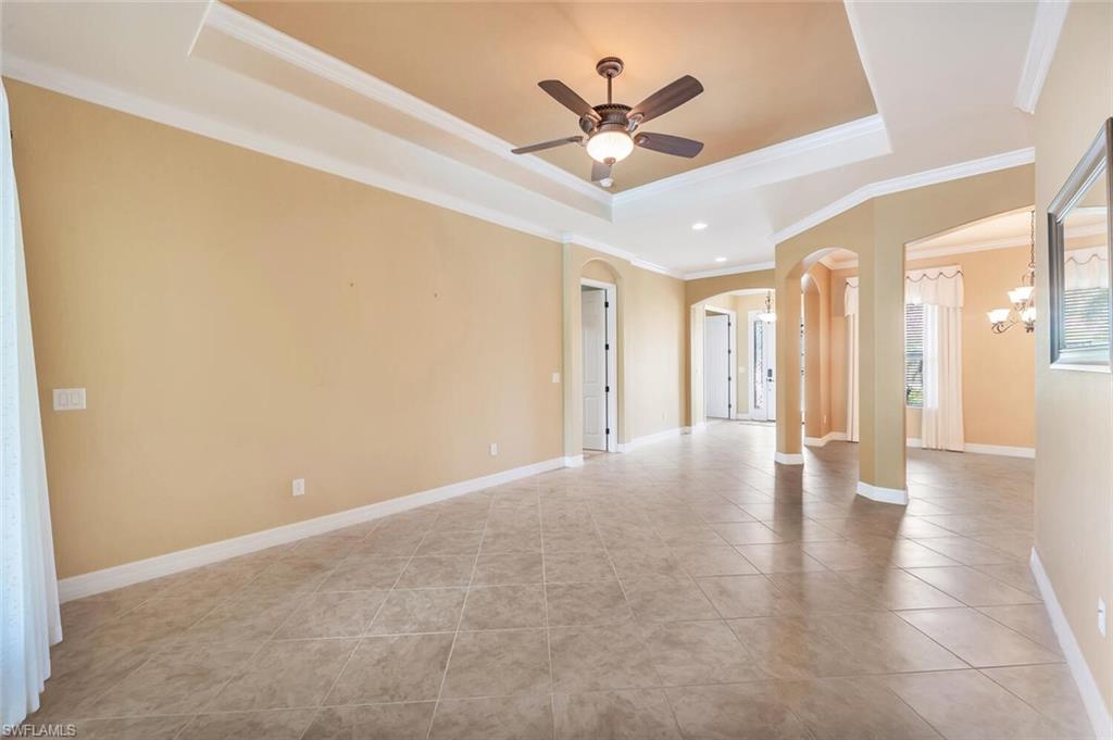 Spacious open-concept living area featuring a tray ceiling with recessed lighting and ceiling fan, neutral wall finishes, tile flooring throughout, and multiple architectural openings that define distinct zones within the space