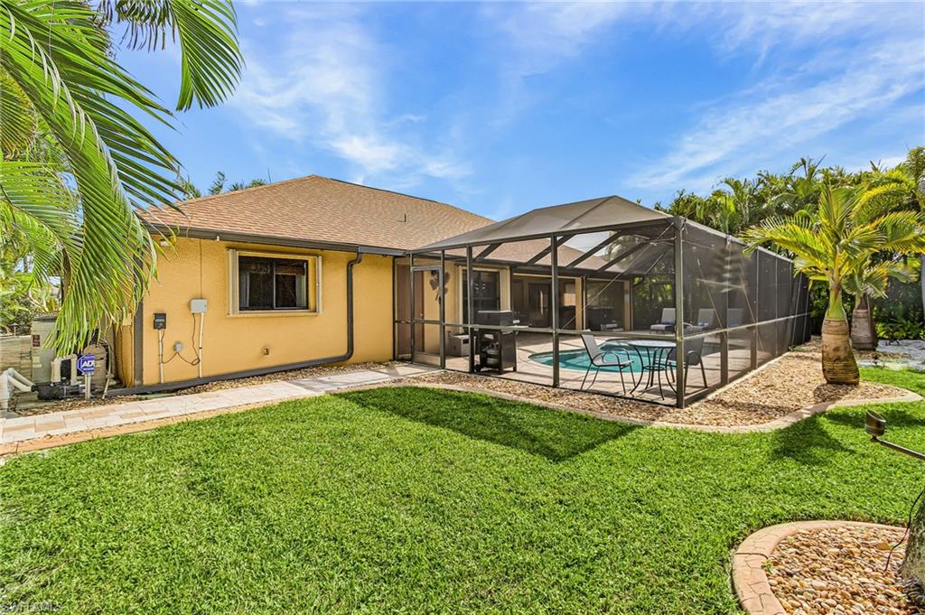 Charming single-story home with a bright yellow stucco exterior and pitched roof, complemented by a spacious screened lanai featuring metal framing and louvered panels