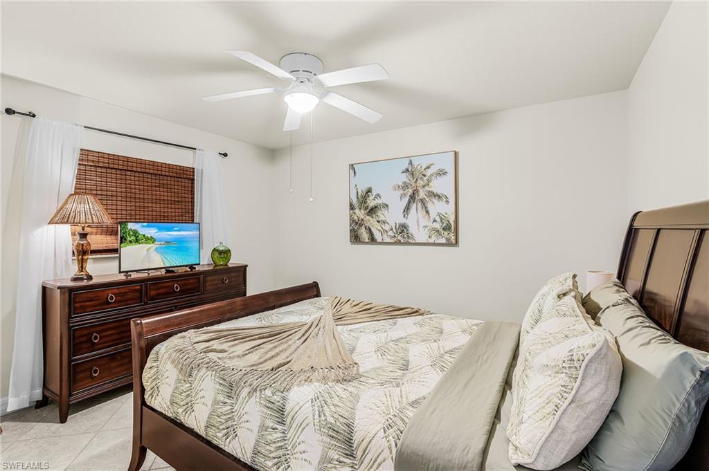 Bedroom featuring a ceiling fan with integrated lighting, a wood-finish bed frame, and tiled flooring