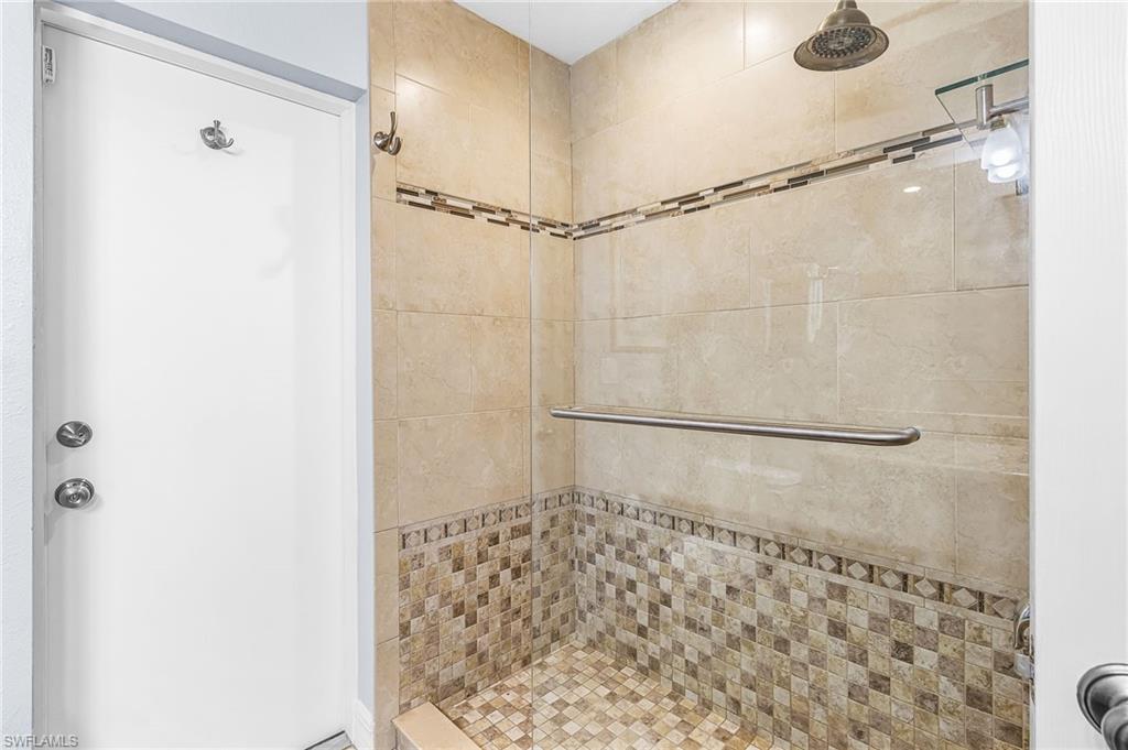 Tiled shower featuring a glass enclosure with a metal handle, a rain showerhead, and a decorative mosaic tile band