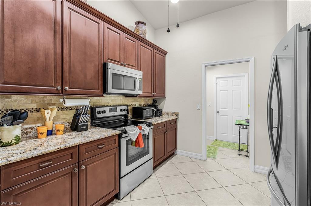 Kitchen featuring dark wood cabinetry, light-toned countertops, stainless steel appliances, a tiled backsplash, and light-colored floor tiling