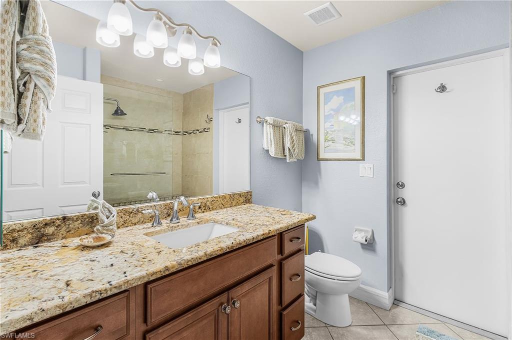 Bathroom vanity featuring a light-toned stone countertop, an undermount sink with a chrome faucet, and a large wall-mounted mirror
