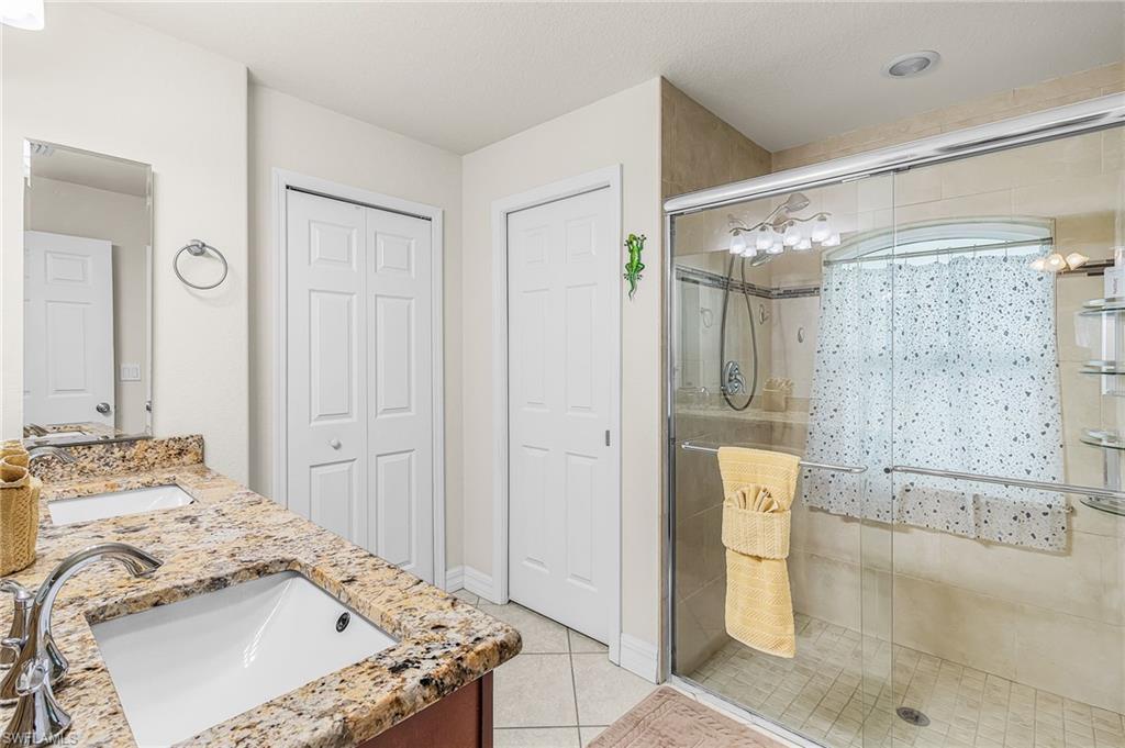 Bathroom featuring a dual vanity with a granite-finish countertop, under-mount sinks, and a walk-in shower with a glass enclosure