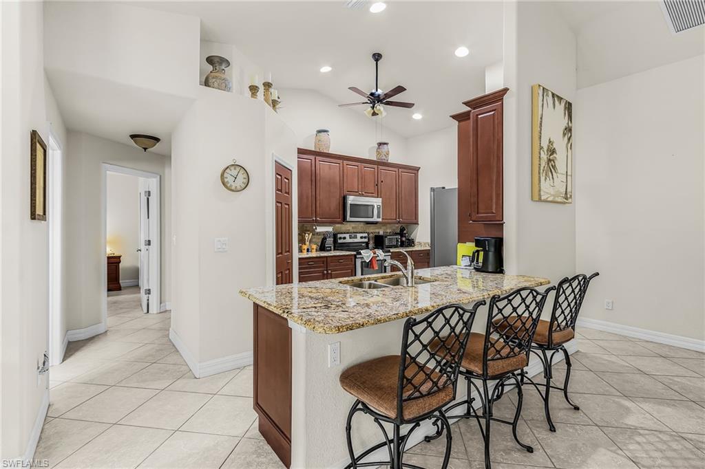 Kitchen featuring a breakfast bar with stone-finish countertop, dark wood-finish cabinetry, stainless-steel appliances, and recessed lighting