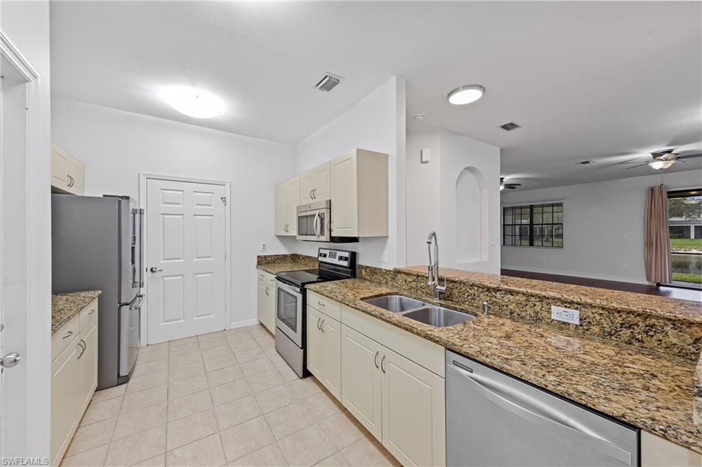 Kitchen with stainless steel appliances, light stone countertops, ceiling fan, and light tile patterned flooring