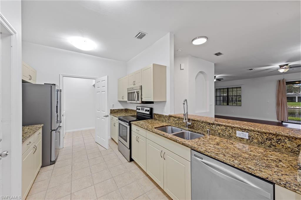 Kitchen with stainless steel appliances, light stone counters, ceiling fan, and light tile patterned floors