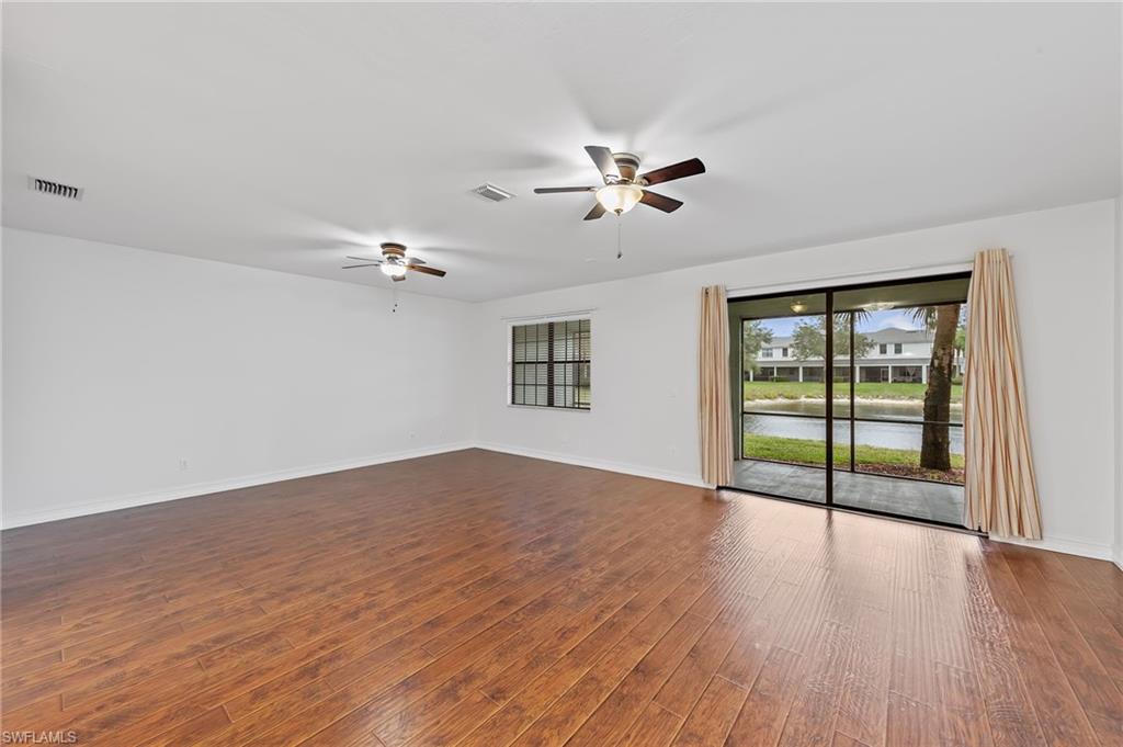 Empty room featuring dark wood-style flooring, a water view, and a ceiling fan