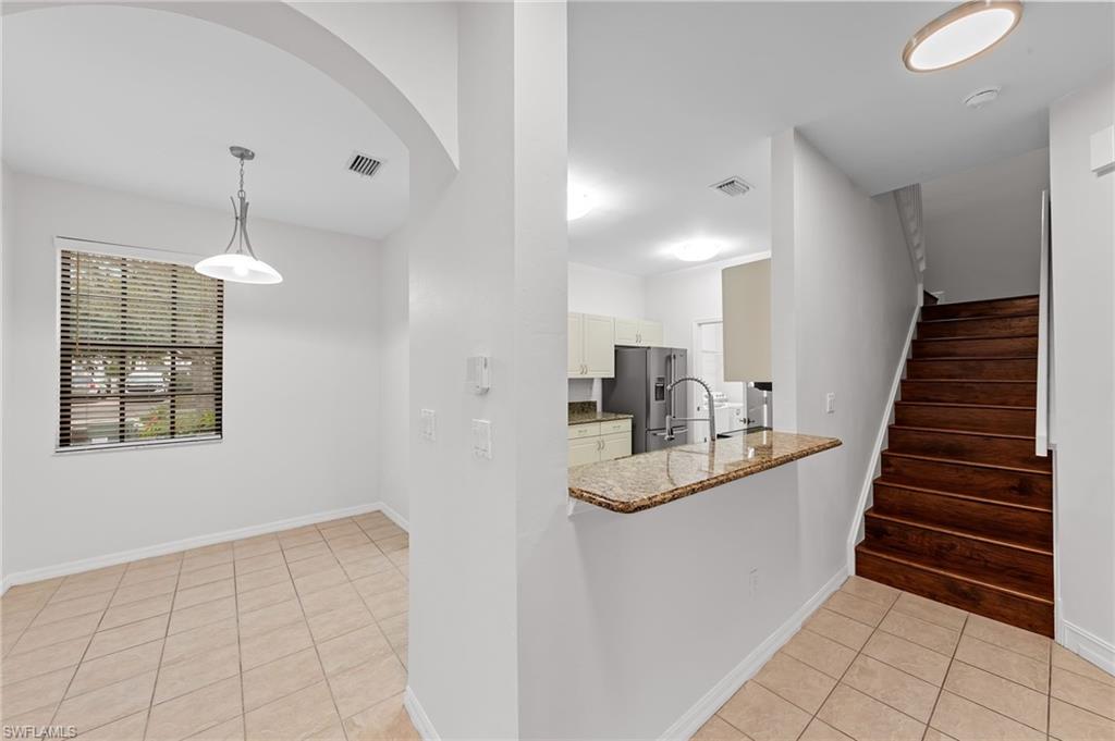 Kitchen with light tile patterned floors, light stone counters, high end fridge, a peninsula, and decorative light fixtures