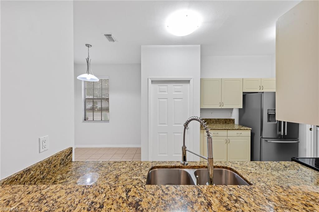 Kitchen with high end refrigerator, dark stone countertops, hanging light fixtures, cream cabinetry, and tile patterned floors