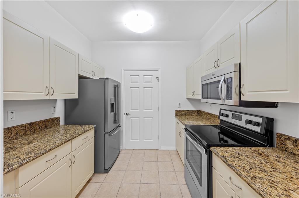 Kitchen with appliances with stainless steel finishes, dark stone countertops, white cabinetry, and light tile patterned floors