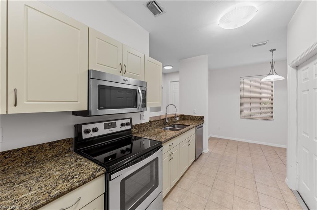 Kitchen featuring appliances with stainless steel finishes, hanging light fixtures, dark stone countertops, and light tile patterned floors