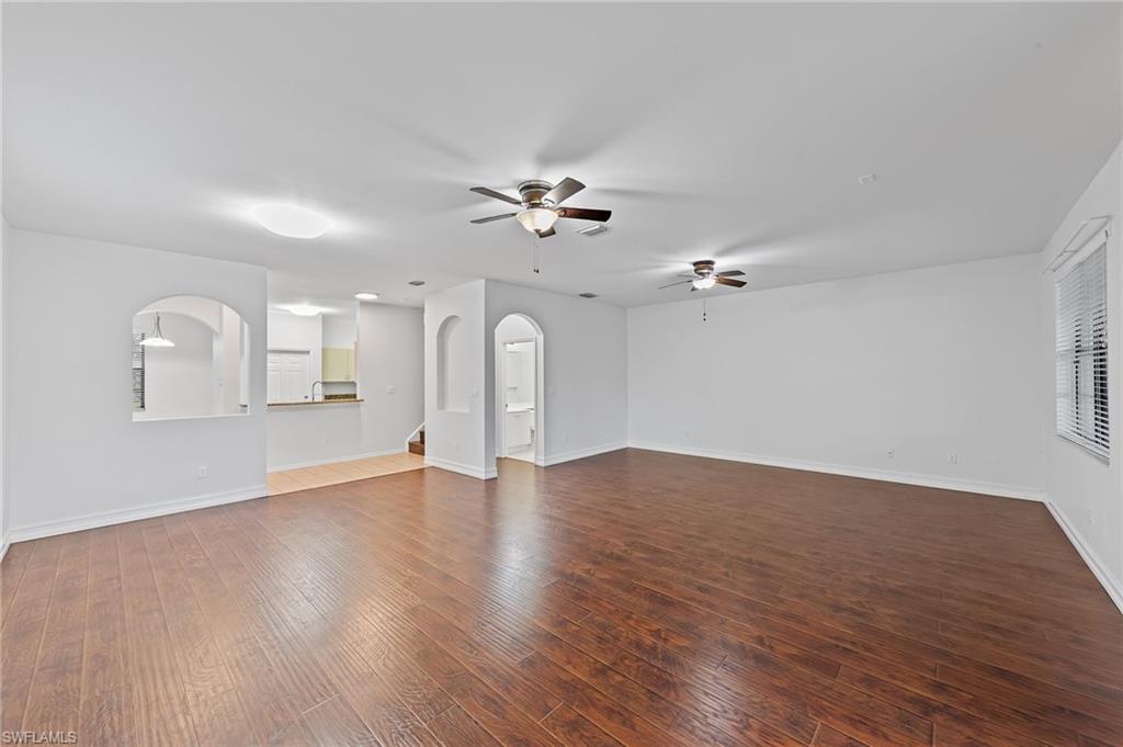 Unfurnished living room with dark wood finished floors, arched walkways, and ceiling fan