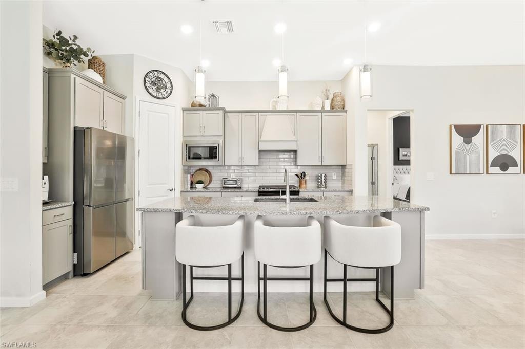Kitchen featuring a large island with a light-toned granite countertop, extensive light gray cabinetry, stainless steel appliances, a white subway tile backsplash, and recessed lighting