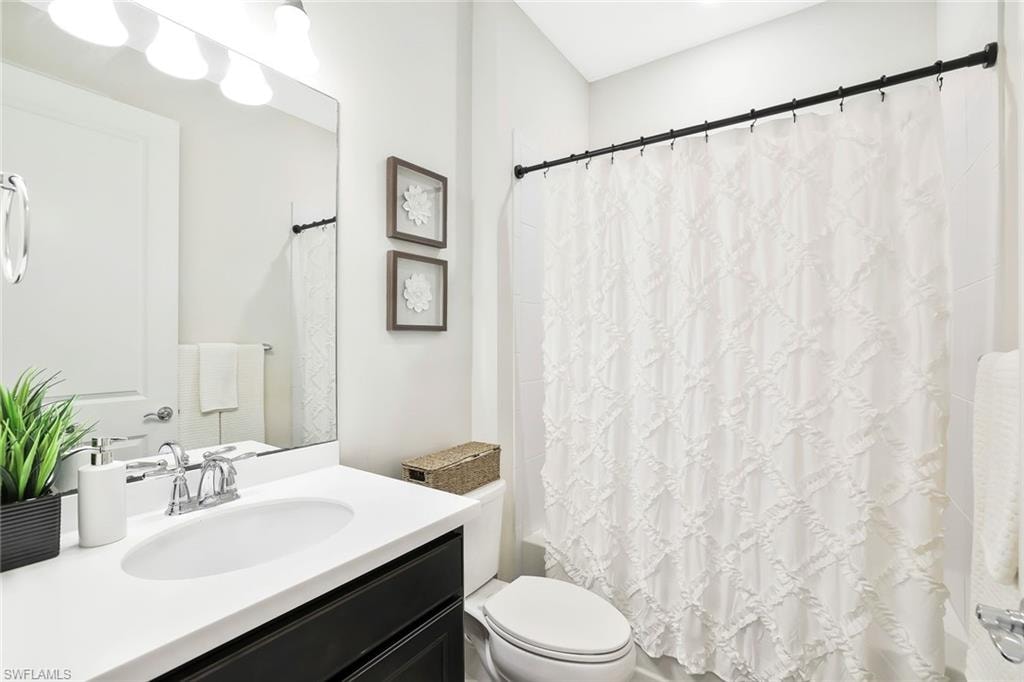 Bathroom featuring a single vanity with a white countertop and dark cabinetry, chrome faucet, wall-mounted mirror, and a toilet