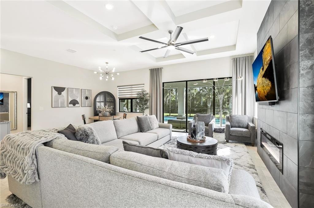Open-concept living area with tray ceiling and contemporary ceiling fan, featuring large format tile flooring, a built-in electric fireplace with a tile surround, and sliding glass doors revealing a patio and pool area