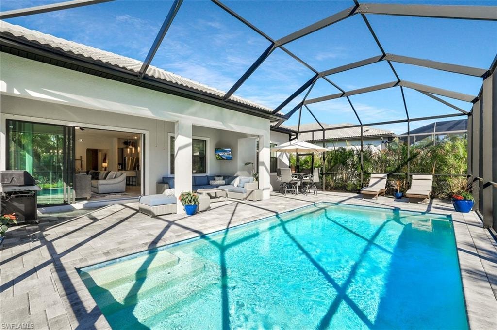 Screened outdoor living area featuring a rectangular pool with steps, expansive paver decking, an extended covered patio, and large sliding glass doors opening to interior spaces