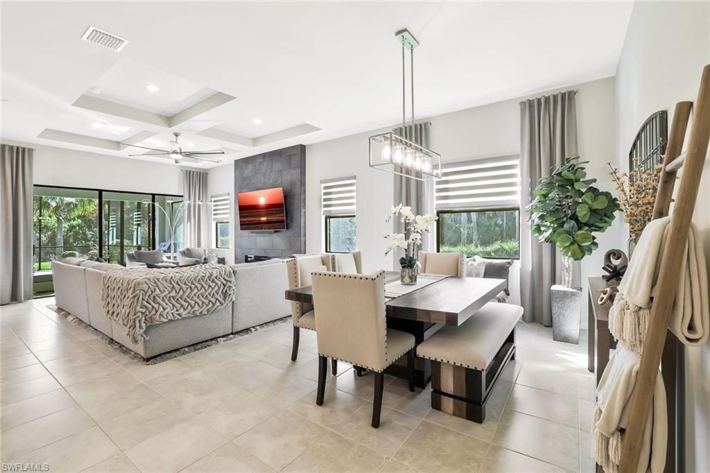 Spacious living area featuring light-toned large format tile flooring, a tray ceiling with a ceiling fan, and sliding glass doors leading to the exterior