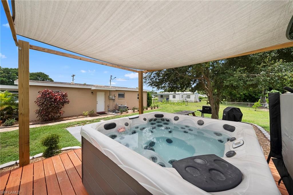 Outdoor spa with a light-colored shade sail structure, set on a wood-finish deck