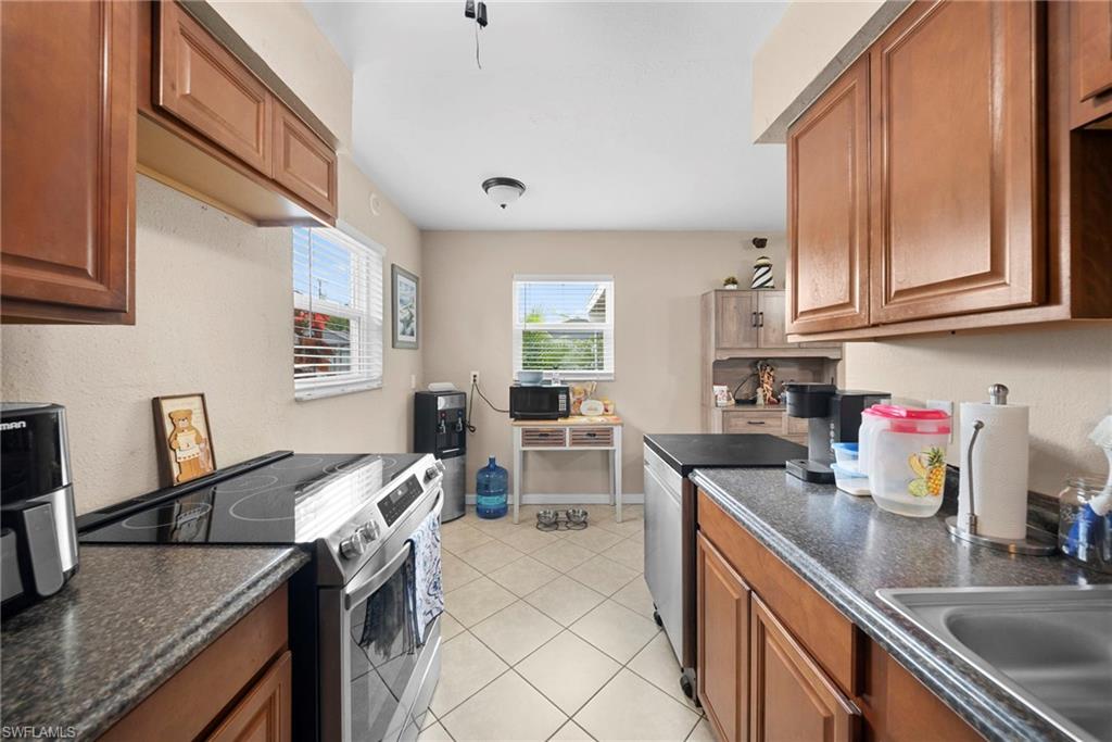 Kitchen featuring abundant wood-finish cabinetry, stone-look countertops, stainless steel appliances, and tile flooring