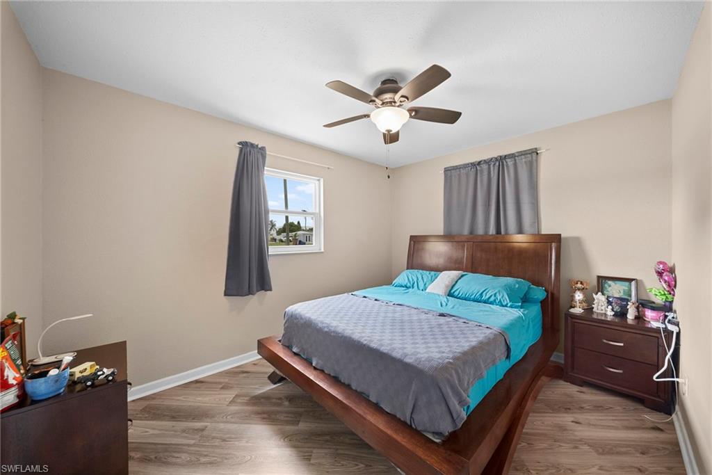 Spacious bedroom showcasing a wood-finish platform bed frame, hardwood flooring, ceiling fan with integrated lighting, and ample natural light from a large window