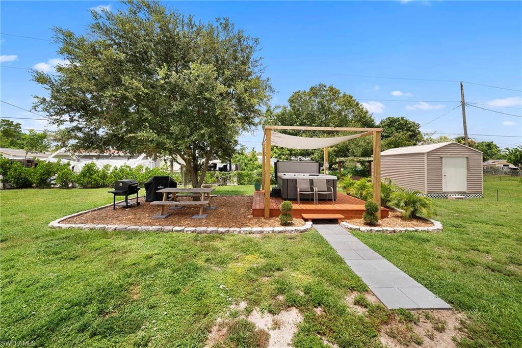 Expansive backyard featuring a hot tub on a raised wood-finish deck with a pergola and sunshade, a separate metal storage shed, a paved pathway, and a bark-mulched entertainment area