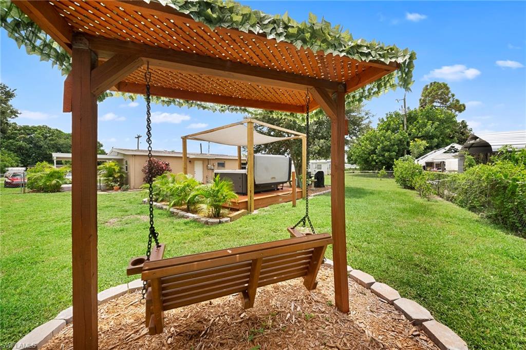 Expansive lawn with a wooden swing under a pergola, a raised wooden deck, and mature landscaping