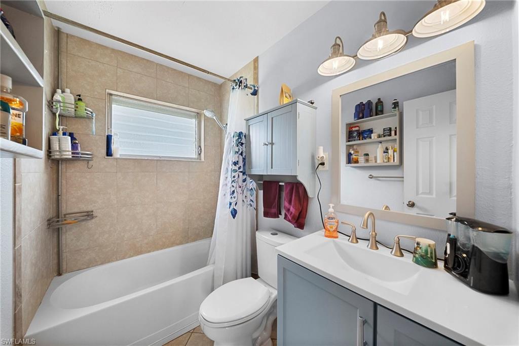 Bathroom featuring a built-in tub with tile surround, a single vanity with an integrated sink, a framed mirror, and a wall-mounted light fixture with three sconces