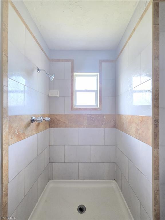Tiled shower stall featuring a window, white subway tiles, and natural stone accent banding