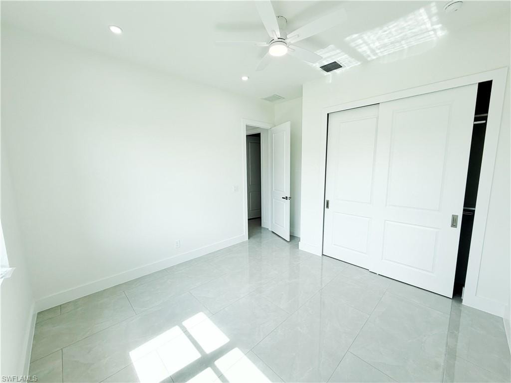Spacious room featuring light-toned tile flooring, white walls, recessed lighting, and a ceiling fan