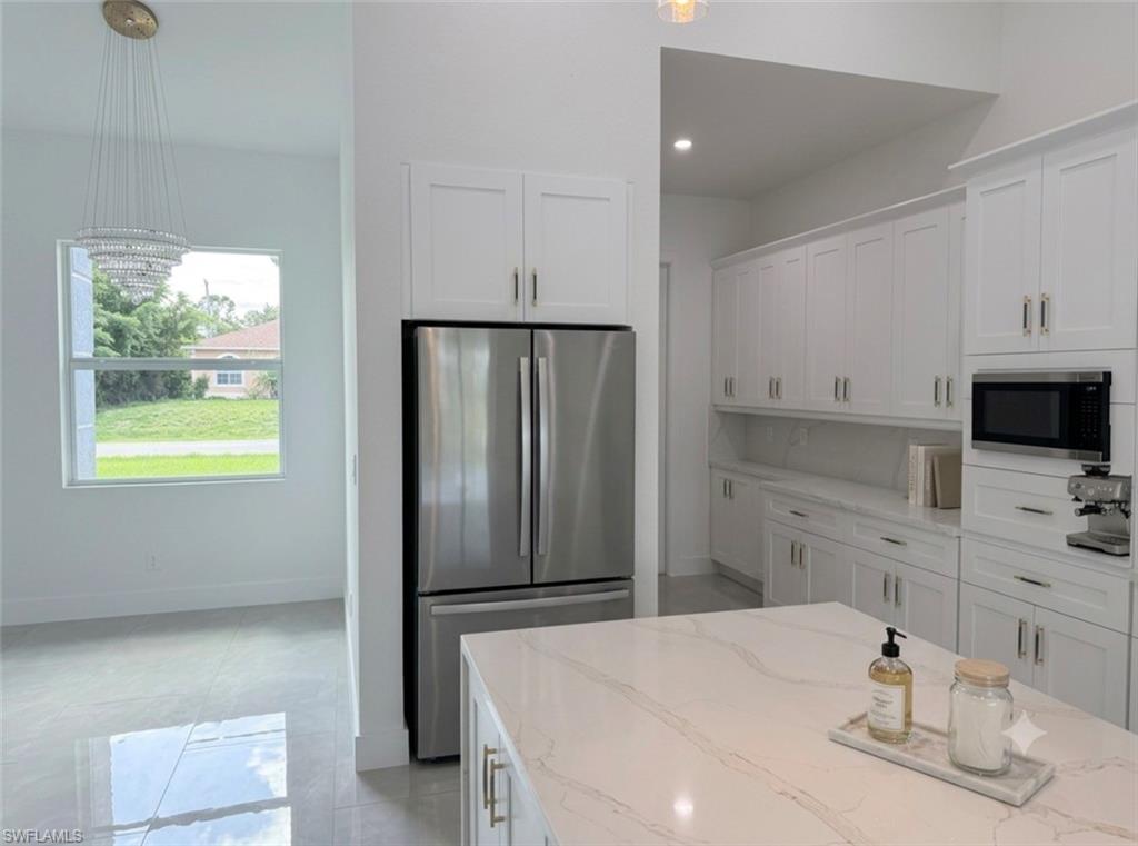 Modern kitchen featuring a large island with a light-toned countertop, extensive white cabinetry, stainless steel appliances, and sleek tile flooring