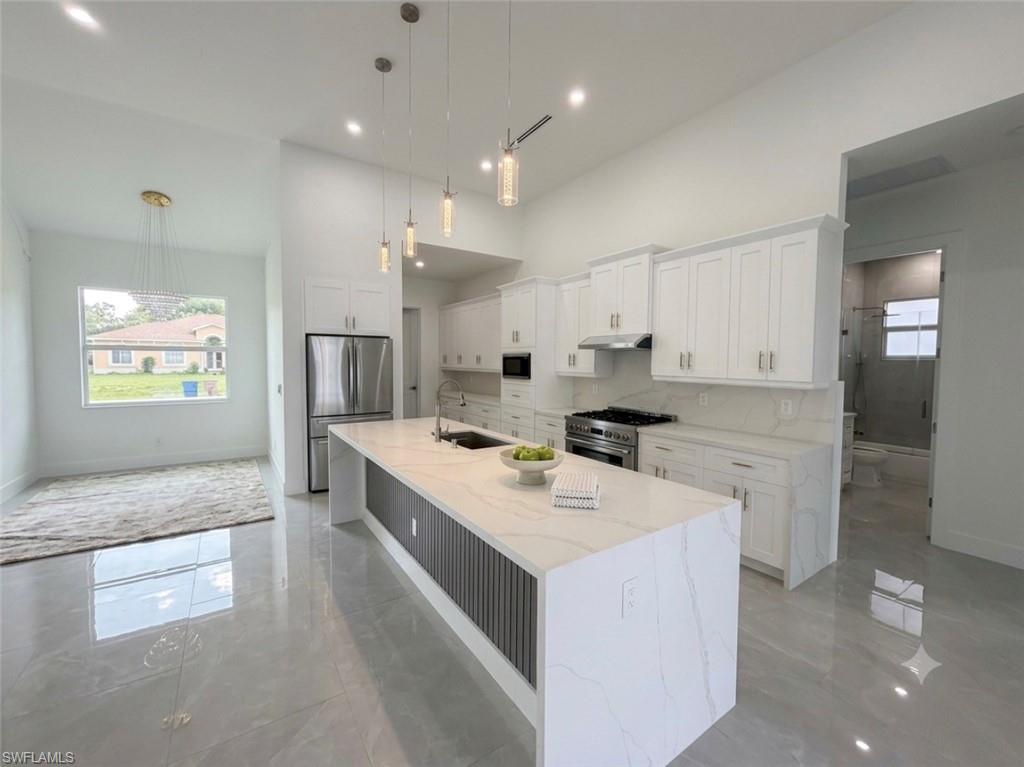 Kitchen with white cabinetry, stainless steel appliances, and a substantial island featuring a white countertop