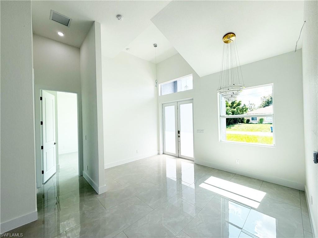 Spacious room featuring vaulted ceilings, a contemporary chandelier, large picture window, and white double French doors