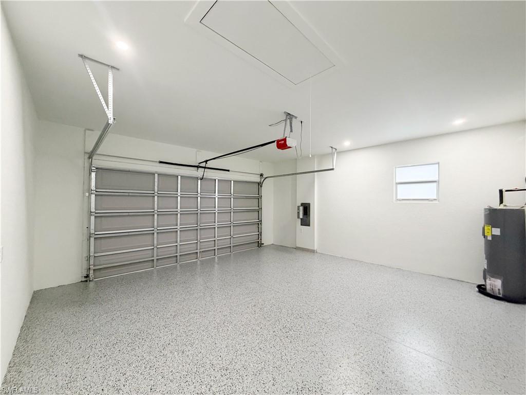 Garage interior featuring a speckled epoxy floor, overhead door, recessed lighting, attic access panel, and a water heater