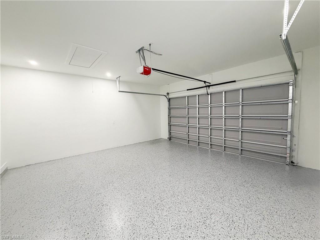 Garage interior featuring a speckled epoxy floor, white walls, recessed ceiling lighting, and an overhead garage door opener