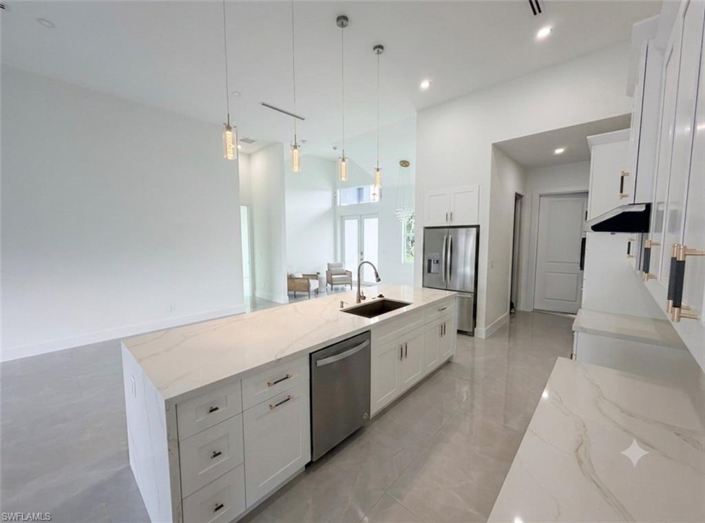 Modern kitchen featuring a large waterfall island with integrated sink, stainless steel appliances, white cabinetry with gold-tone hardware, and recessed lighting