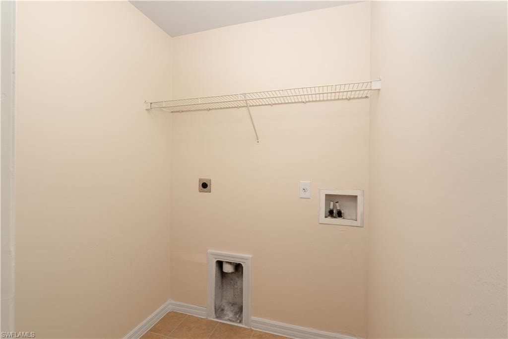 Dedicated laundry area featuring a wire shelf, wall-mounted electrical outlet, water hookups, and a floor drain